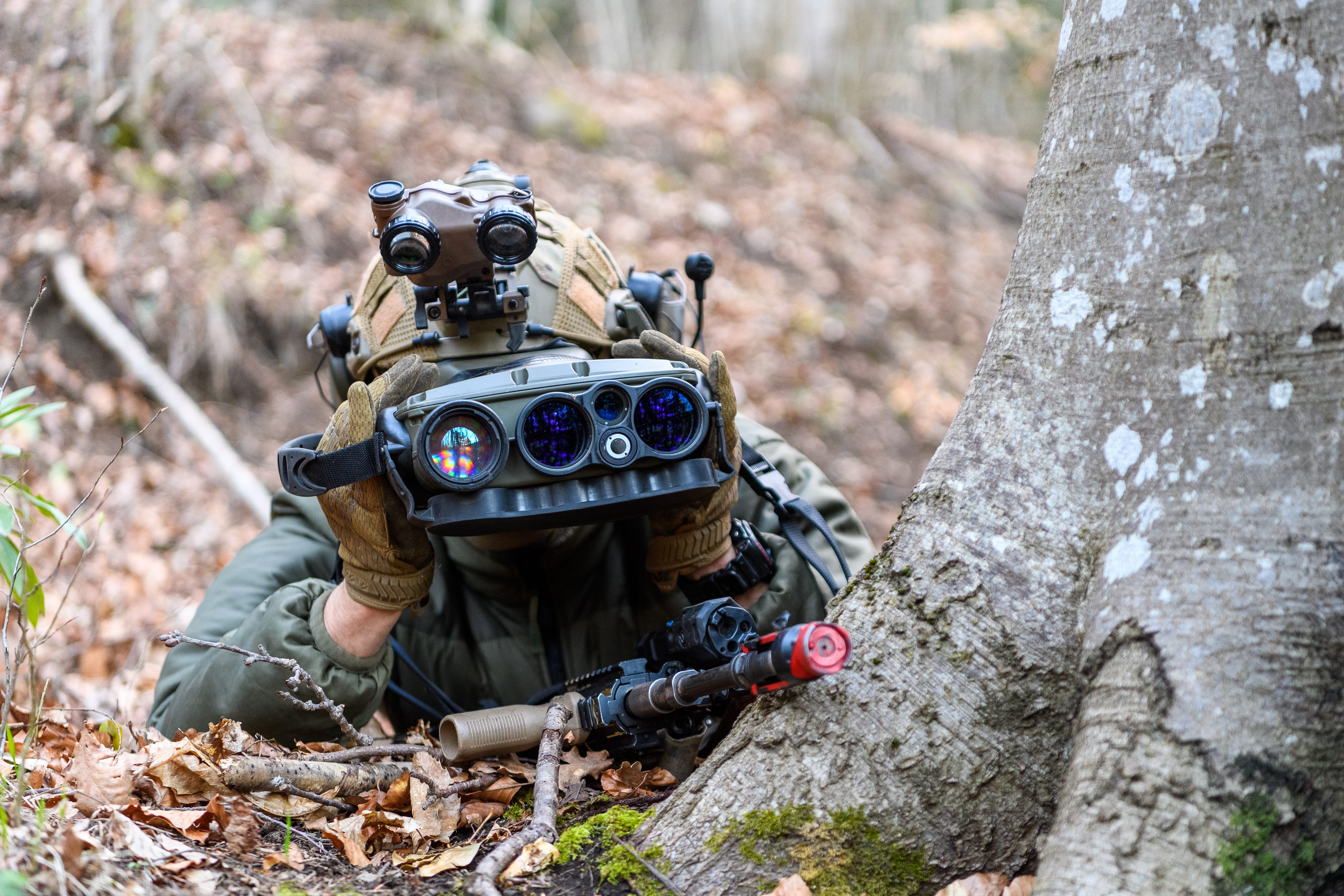 Soldier with IR binoculars hidden behind a tree